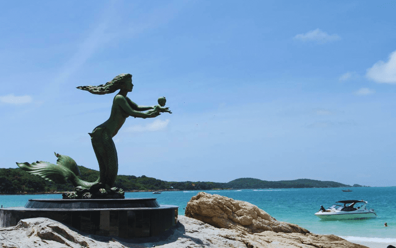 Statue de sirène sur la plage de Koh Samet en Thaïlande avec vue sur la mer turquoise et un bateau au loin