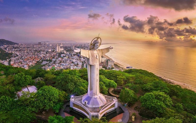 Statue monumentale du Christ Rédempteur à Vung Tau, dominant la ville et le littoral, entourée de verdure avec une vue panoramique sur la mer au coucher du soleil