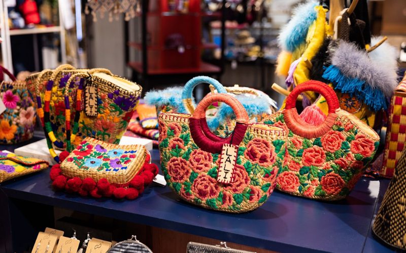 Paniers artisanaux thaïlandais colorés en osier décorés de broderies florales vives et de pompons, exposés sur un étal de marché ou une boutique de souvenirs