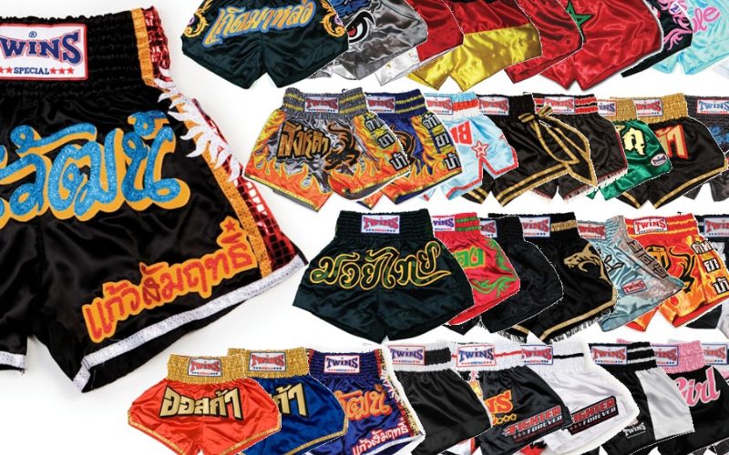Collection de shorts de Muay Thaï colorés et décorés de motifs traditionnels et d’inscriptions thaïlandaises, disposés en plusieurs rangées, utilisés pour l’entraînement et les combats de boxe thaïlandaise
