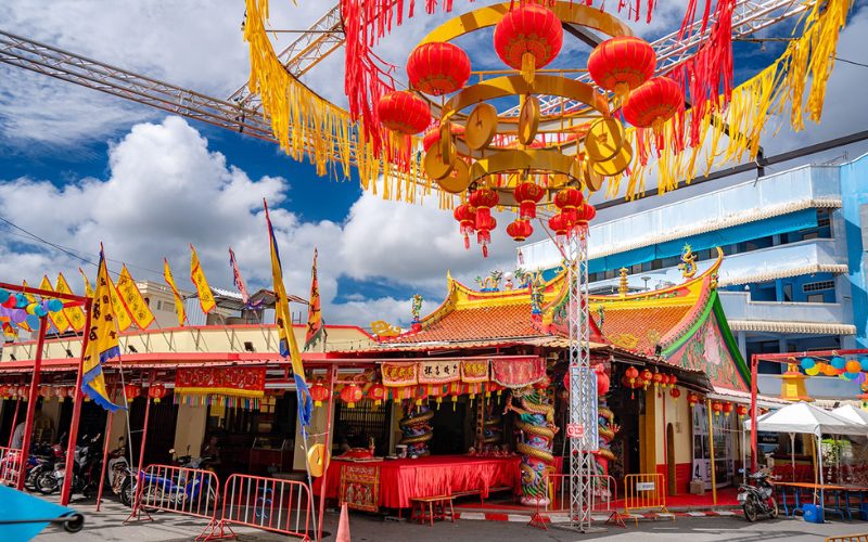 Temple chinois richement décoré à Phuket pendant le festival Por Tor, orné de lanternes rouges, de bannières jaunes et de rubans colorés sous un ciel bleu éclatant