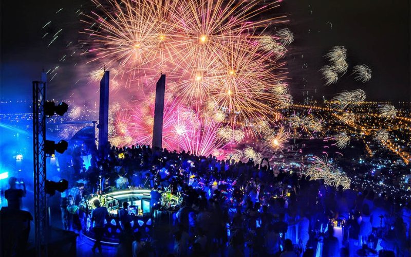 Spectateurs réunis dans une ambiance festive sur un rooftop à Da Nang, profitant d’une vue spectaculaire sur un ciel illuminé par des feux d’artifice éclatants, avec en toile de fond la ville scintillante de nuit