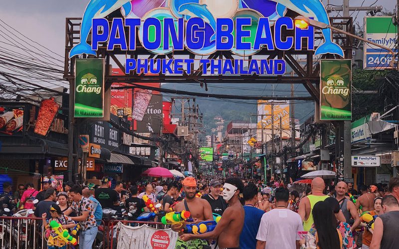 Foule animée célébrant Songkran sous l’enseigne lumineuse de Patong Beach à Phuket, avec des participants tenant des pistolets à eau colorés dans une ambiance festive de rue
