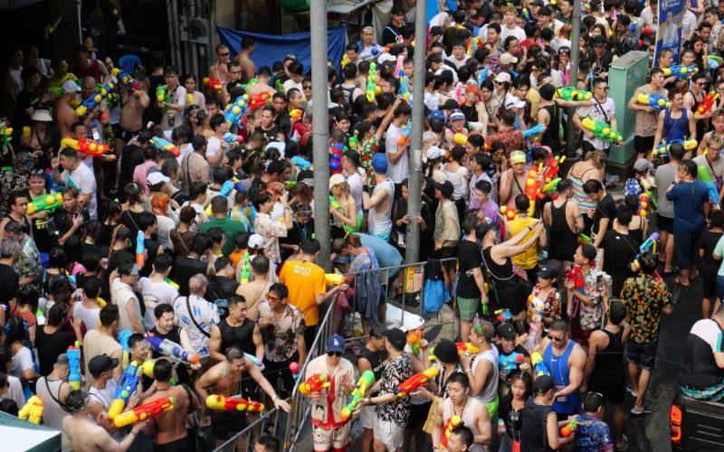 Foule dense de participants célébrant le festival de Songkran dans une rue de Bangkok, armés de pistolets à eau colorés et s’aspergeant joyeusement au cœur de l’ambiance festive
