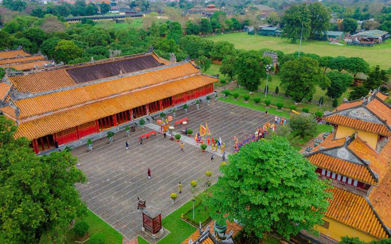 Vue aérienne du Temple The Mieu dans la Cité impériale de Hué, avec sa grande cour pavée où se déroule une cérémonie traditionnelle en costume, entourée de bâtiments anciens aux toits de tuiles orange et d’un vaste jardin verdoyant