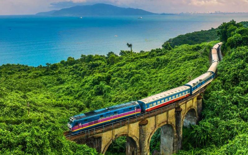Train reliant Hanoï à Hué traversant un pont au-dessus d’une vallée verdoyante, avec vue panoramique sur la mer au loin