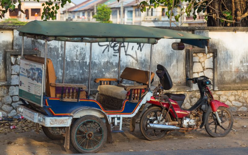 Tuk-tuk cambodgien traditionnel avec remorque en bois et toit en toile, attaché à une moto, prêt à transporter des passagers dans les rues de Kampot