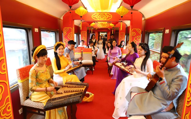Des musiciens et musiciennes en tenue traditionnelle vietnamienne jouent d’instruments folkloriques à bord d’un train décoré aux couleurs rouges et or