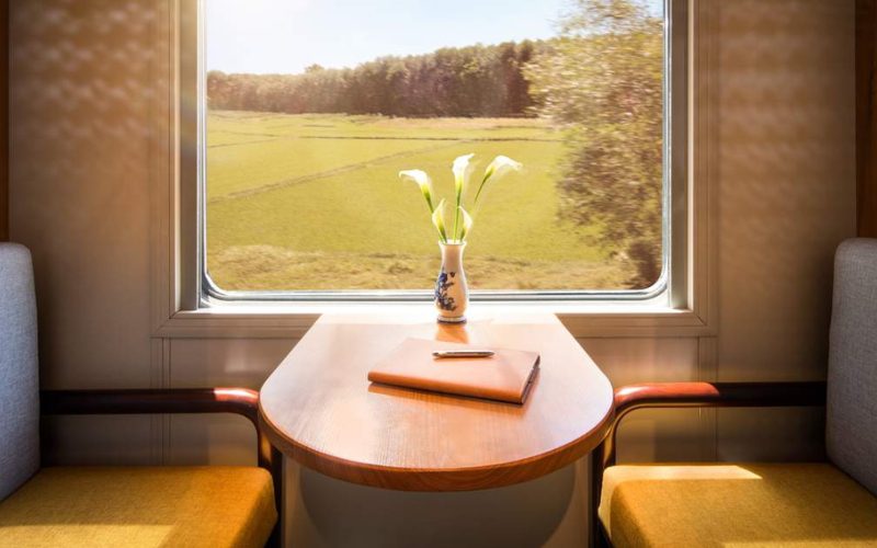 Table en bois élégante à bord d’un train vietnamien, décorée d’un vase de fleurs et d’un carnet, avec vue sur les rizières ensoleillées à travers la fenêtre