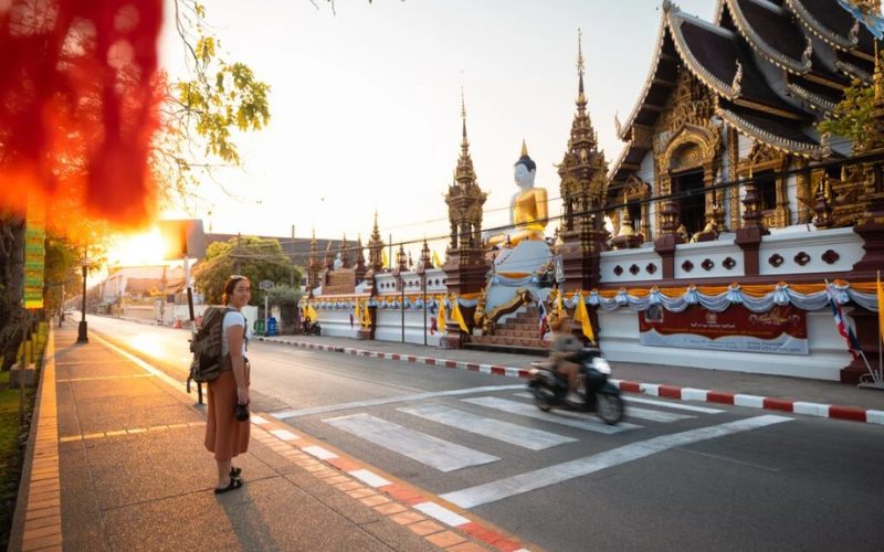 Voyageuse marchant devant un temple bouddhiste à Chiang Mai au coucher du soleil, avec statue de Bouddha, architecture traditionnelle et rue animée