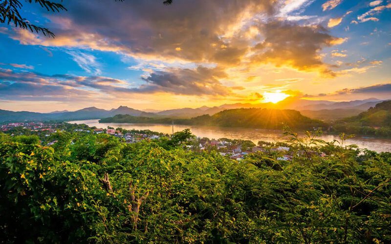 Coucher de soleil spectaculaire sur le Mékong à Luang Prabang, avec des collines verdoyantes et des nuages colorés illuminés par la lumière dorée du soir