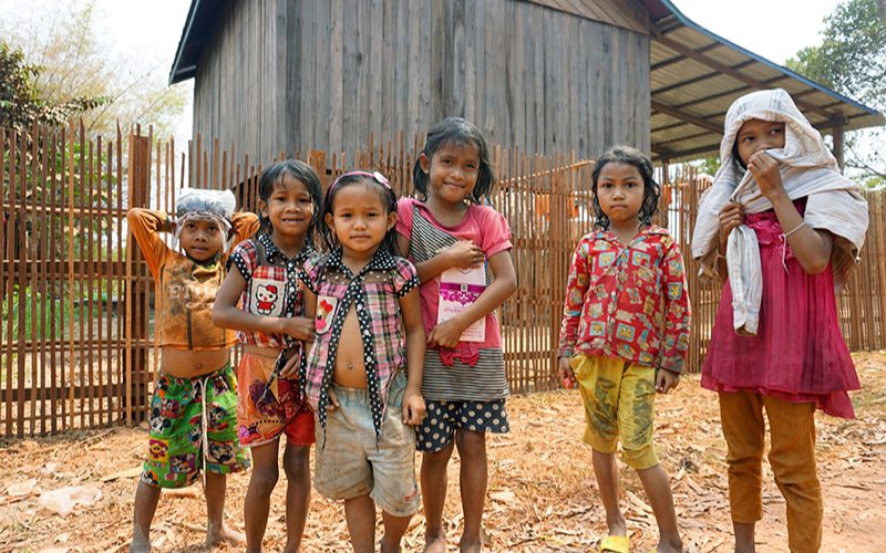 Groupe d’enfants souriants d’un village rural au Cambodge, debout devant une maison en bois traditionnelle