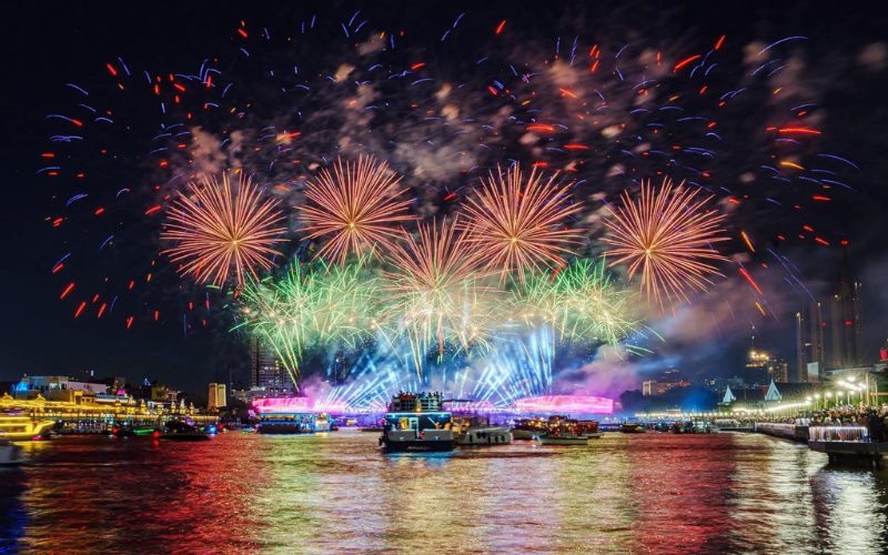 Feu d’artifice spectaculaire illuminant le ciel nocturne au-dessus de la rivière Chao Phraya à Bangkok, avec des bateaux colorés naviguant sur l’eau et les reflets lumineux se mêlant aux installations du festival