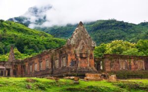 Ruines du temple de Wat Phou au Laos, ancien sanctuaire khmer en pierre entouré de verdure luxuriante, avec montagnes et brume en arrière-plan