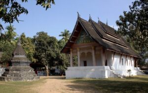 Temple traditionnel laotien à Luang Prabang, entouré de végétation luxuriante, avec un stupa en pierre à proximité, reflétant l'architecture bouddhiste locale