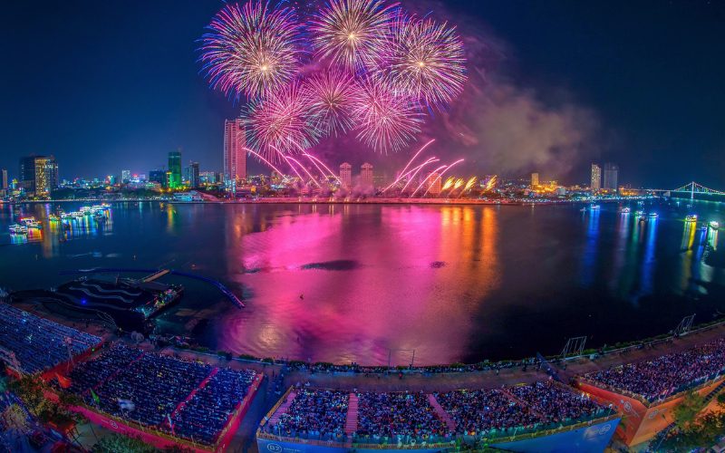 Vue panoramique spectaculaire du Festival International de Feux d’Artifice de Da Nang, avec des feux multicolores illuminant le ciel nocturne au-dessus de la rivière Hàn, reflétés dans l’eau
